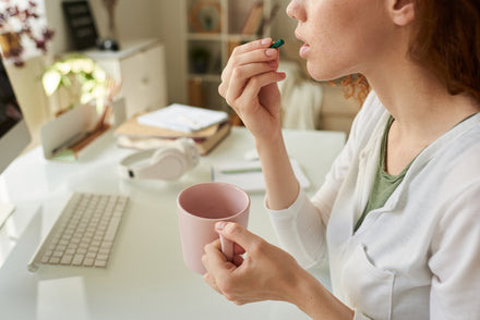 woman taking supplements with a pink mug of tea