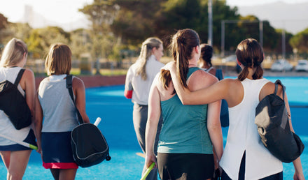 women teammates walking away from the camera, arm-in-arm, supporting one another after a field hockey practice